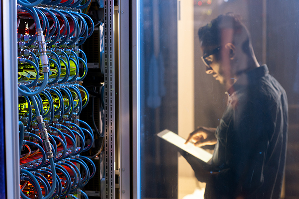 Photo of a man examining a tablet computer with a rack sprouting blue cables in the foreground